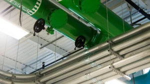 Tubulação verde de grande diâmetro com válvulas de volante e eletrodutos metálicos correndo no teto de uma instalação industrial